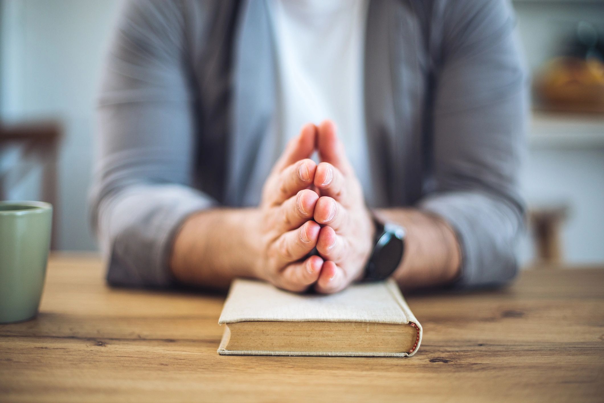 Hands clasped in prayer on a closed Bible